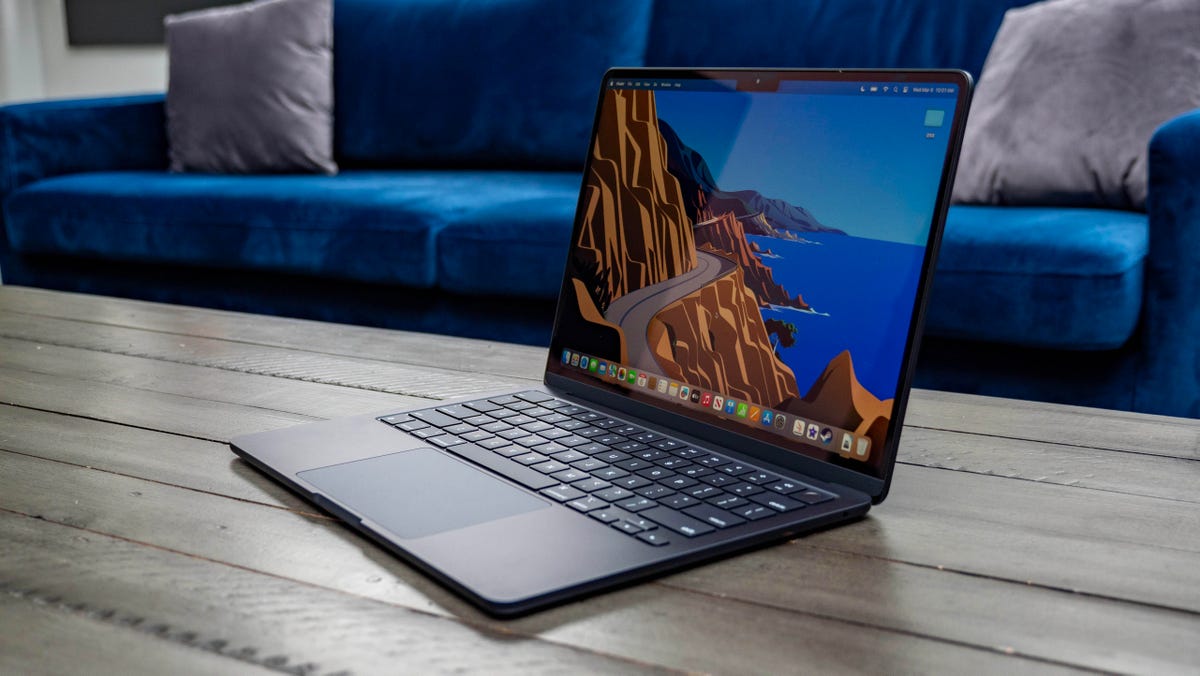 Apple MacBook Air M3 13-inch laptop on a wood table with a blue couch in the background.