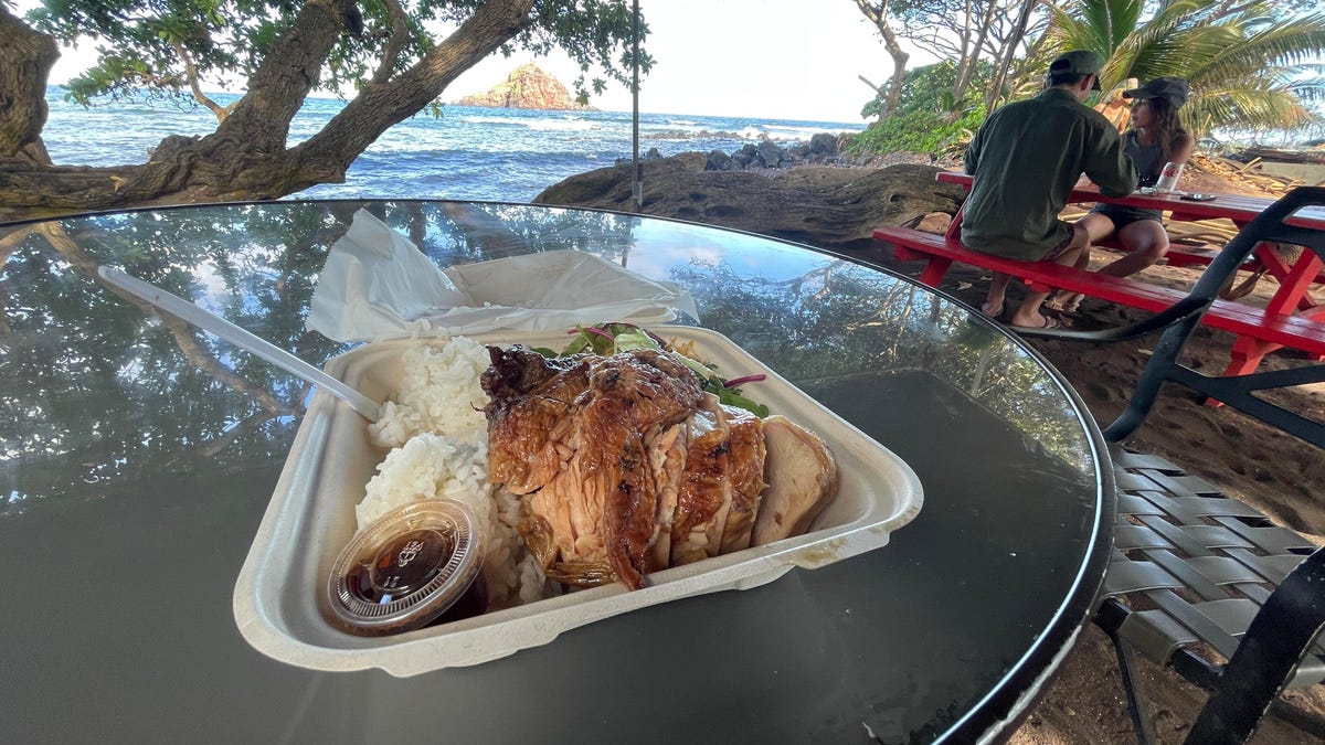 A plate of chicken on a table overlooking Koki Beach. The chicken looks spectacular, grilled to smoky yet moist perfection. It comes with a signature spicy vinegar sauce that's to die for. Sticky rice and a salad with miso dressing is behind it.