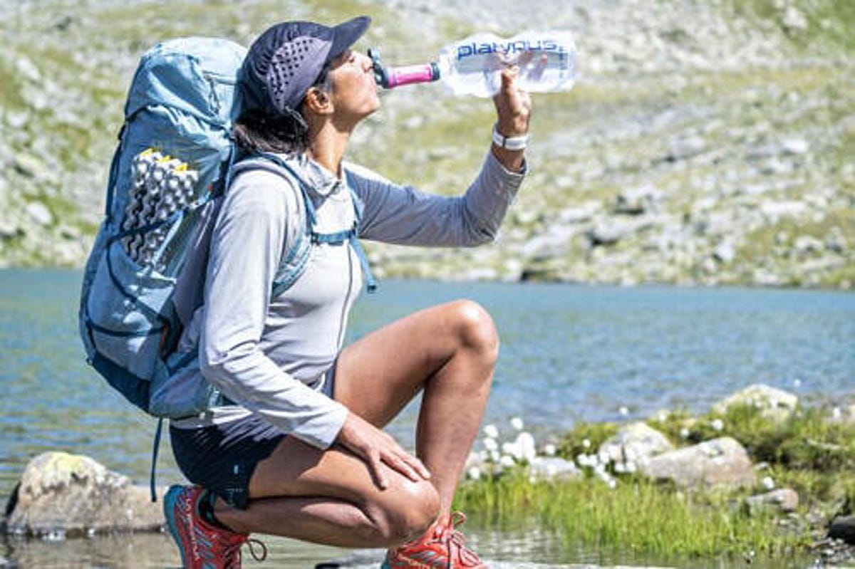 A hiking woman using a filter to drink from a Platypus soft bottle.