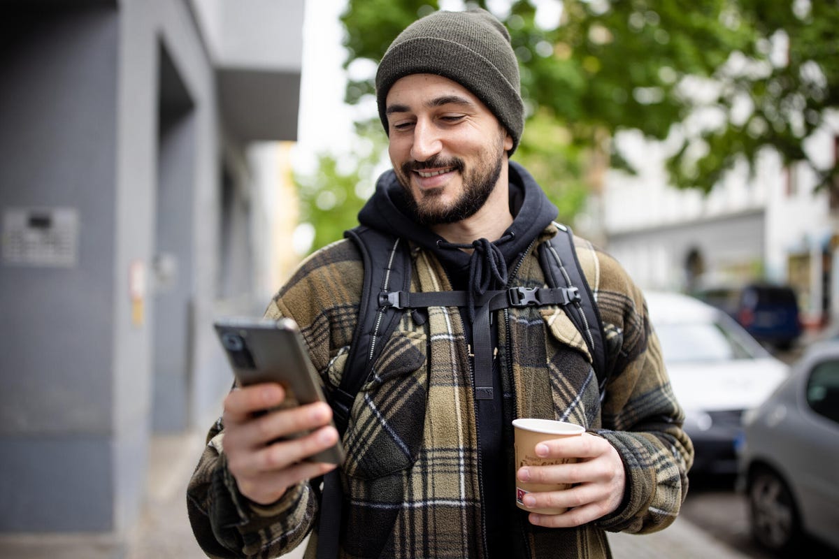 A man in cold weather clothing uses phone to post content outside on the street.